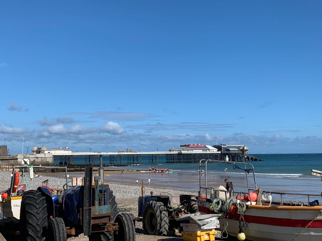 Cromer Pier, Norfolk, UK set in the sunshine against a blue sky.  Taken from the beach with the fisherman's tractors and boats in the foreground.